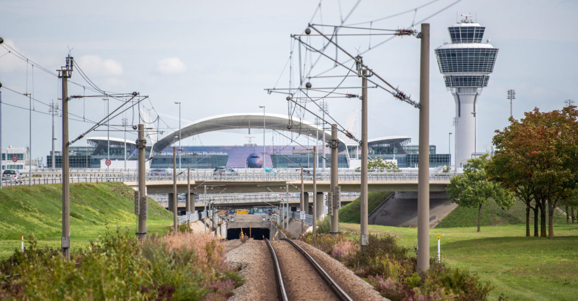 Leere Gleise führen zum Flughafen München mit dem Tower im Hintergrund.